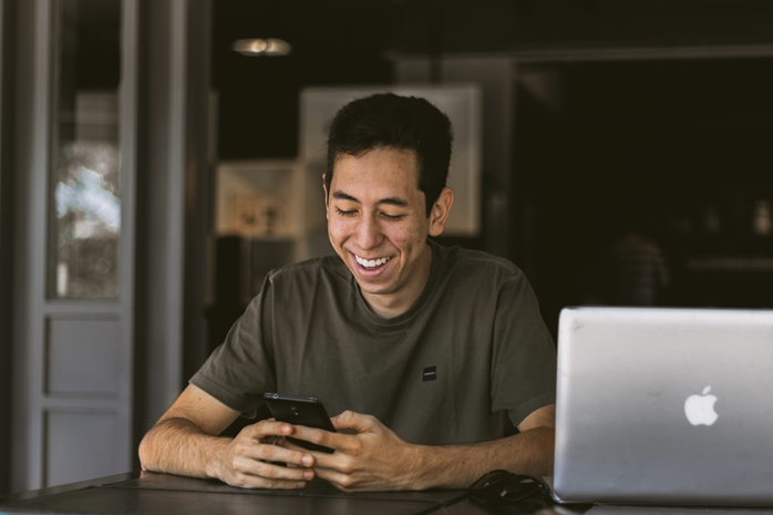 homem de camiseta verde sorrindo ao celular sentado a mesa ao lado no laptop cinza.
A satisfação no trabalho tem um grande efeito na qualidade de sua vida.