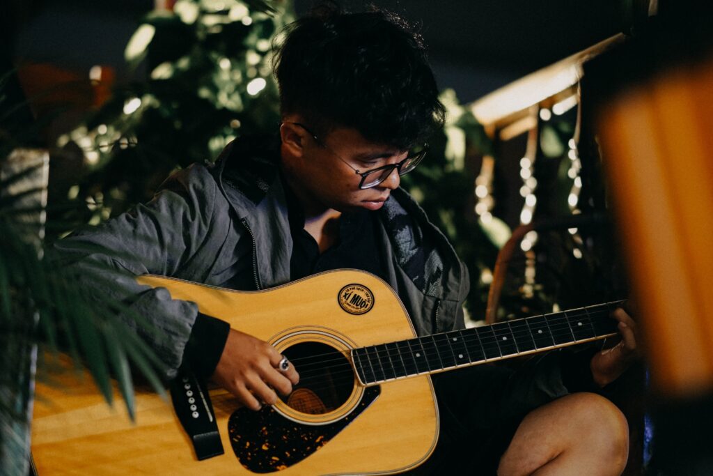 Rapaz sentado tocando violão usando óculos e jaqueta cinza.
Invista em talvez, aprender algo novo, como tocar violão.